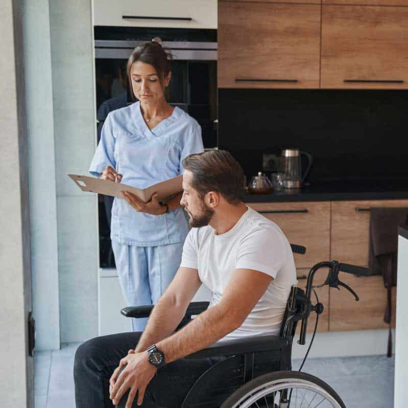 Female nurse assisting a male patient in a wheel chair.