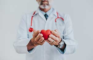 Doctor in a white dress robe holding a red foam heart.